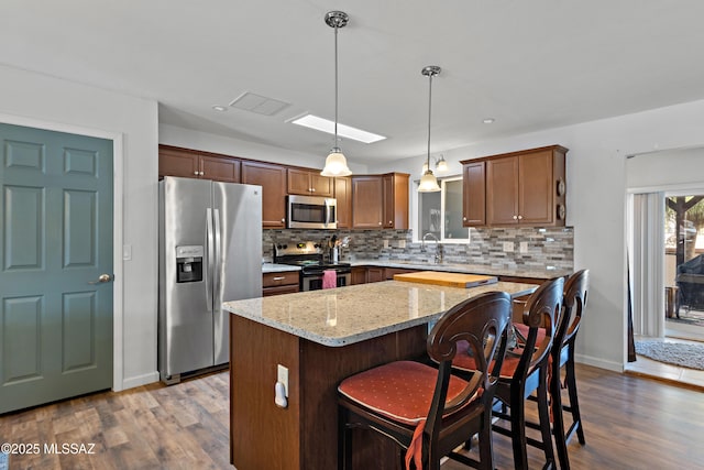 kitchen featuring stainless steel appliances, dark wood-style flooring, decorative backsplash, light stone countertops, and a kitchen bar