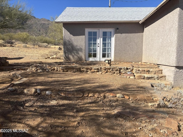 view of home's exterior with french doors, roof with shingles, and stucco siding