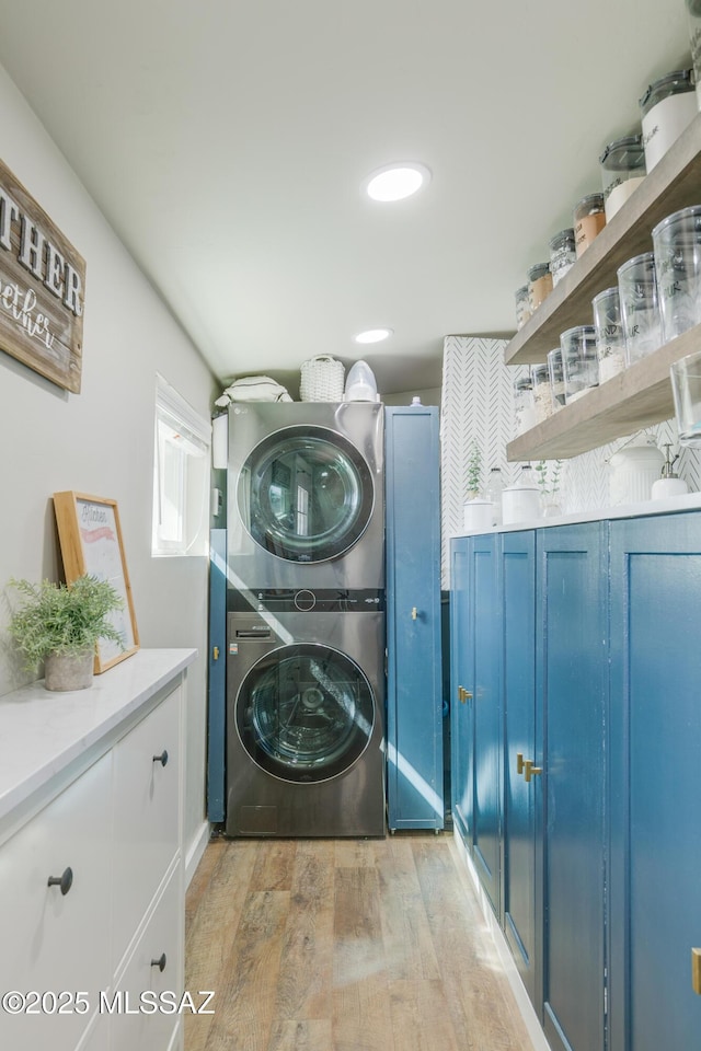 laundry room featuring light wood-type flooring, cabinet space, and stacked washer and clothes dryer