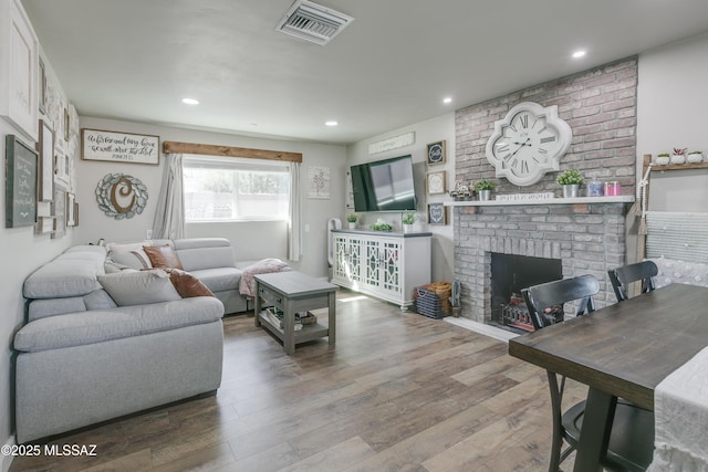 living room with a brick fireplace, wood finished floors, visible vents, and recessed lighting