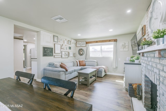 living area featuring recessed lighting, visible vents, a brick fireplace, wood finished floors, and baseboards