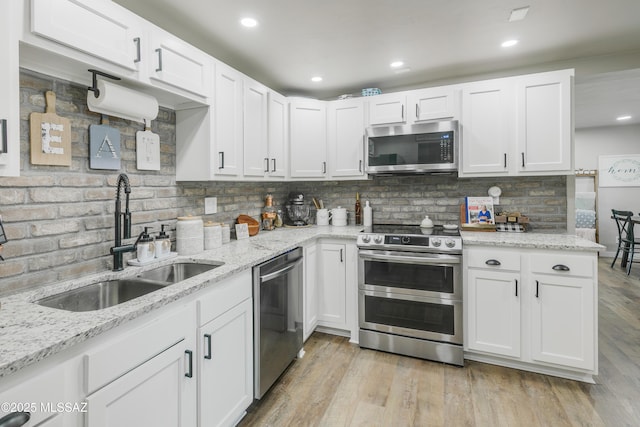 kitchen with stainless steel appliances, light wood-type flooring, white cabinetry, and a sink