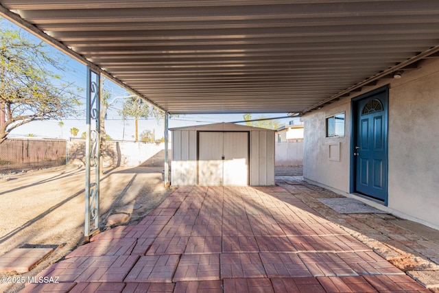 view of patio / terrace with a carport, fence, an outdoor structure, and a storage unit