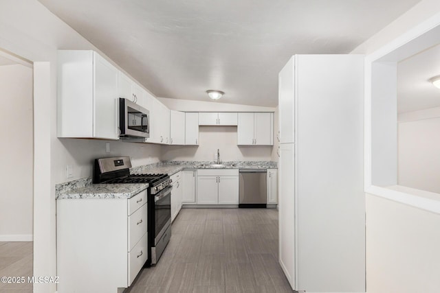 kitchen with white cabinets, appliances with stainless steel finishes, light stone countertops, light wood-style floors, and a sink