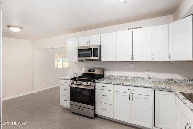 kitchen with light stone counters, stainless steel appliances, visible vents, white cabinetry, and baseboards