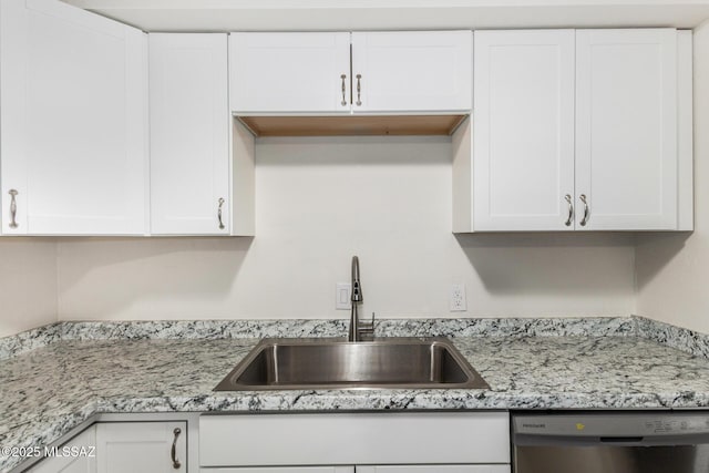 kitchen featuring stainless steel dishwasher, a sink, light stone countertops, and white cabinets