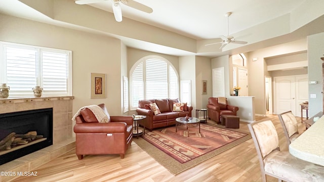 living room with light wood finished floors, a tiled fireplace, and a ceiling fan