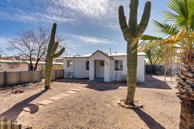 rear view of property featuring a gate, fence, and stucco siding