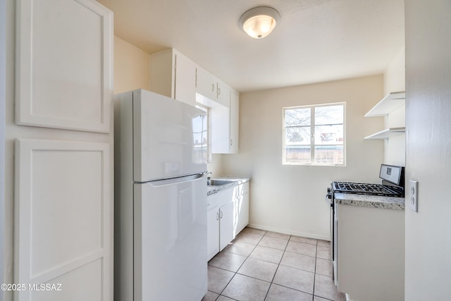 kitchen with open shelves, light tile patterned floors, freestanding refrigerator, white cabinets, and stainless steel range with gas stovetop