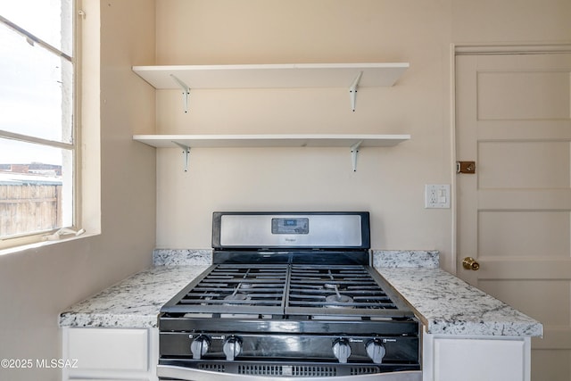 room details with light stone counters, white cabinets, stainless steel gas stove, and open shelves