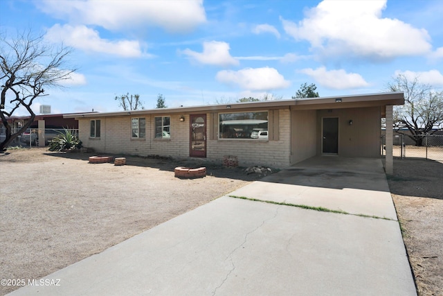 ranch-style house featuring brick siding, concrete driveway, a carport, and fence