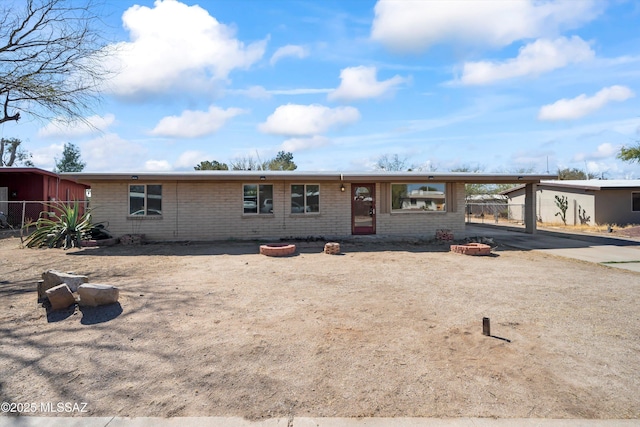 ranch-style house with a carport, concrete driveway, a fire pit, and brick siding