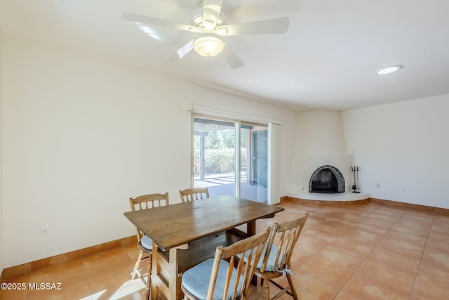 dining room featuring ceiling fan, a fireplace, baseboards, and light tile patterned floors