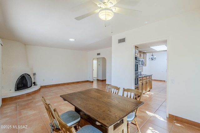 dining room featuring arched walkways, light tile patterned floors, visible vents, a large fireplace, and ceiling fan