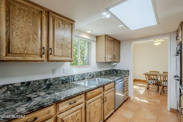 kitchen with light tile patterned floors, a skylight, a sink, stainless steel dishwasher, and black oven