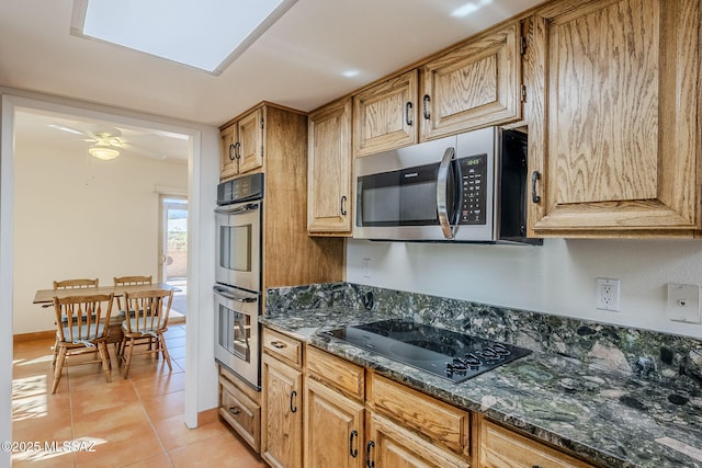 kitchen featuring appliances with stainless steel finishes, a ceiling fan, light tile patterned flooring, dark stone countertops, and baseboards