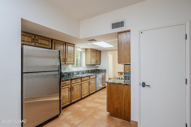 kitchen with light tile patterned floors, stainless steel appliances, a sink, visible vents, and brown cabinets