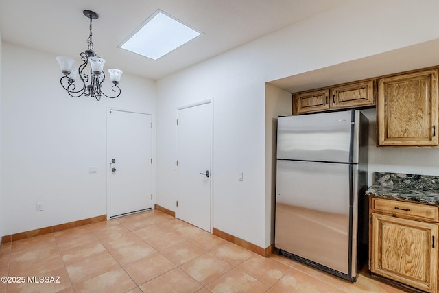 kitchen with decorative light fixtures, light tile patterned floors, brown cabinetry, freestanding refrigerator, and baseboards