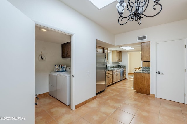 kitchen featuring brown cabinets, washing machine and clothes dryer, stainless steel appliances, visible vents, and an inviting chandelier