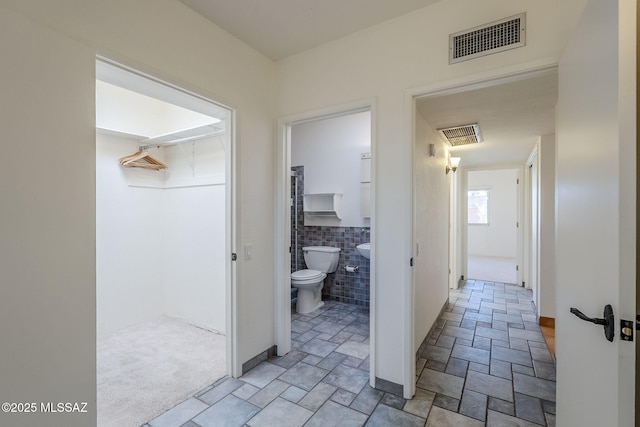 hallway featuring light carpet, stone finish floor, visible vents, and tile walls