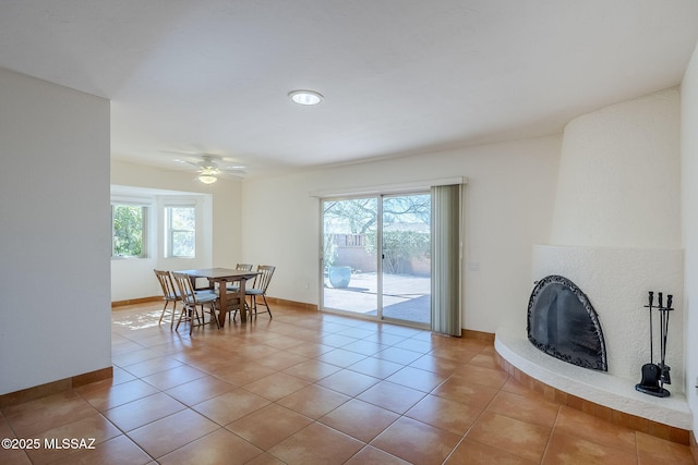 tiled dining room with a fireplace, baseboards, and ceiling fan