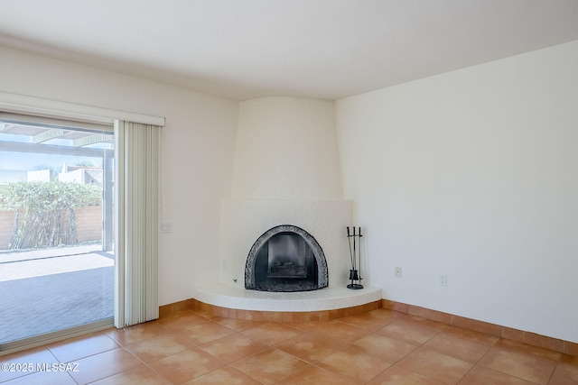 unfurnished living room with a fireplace, baseboards, and light tile patterned flooring