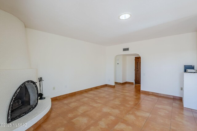 unfurnished living room with baseboards, visible vents, and arched walkways