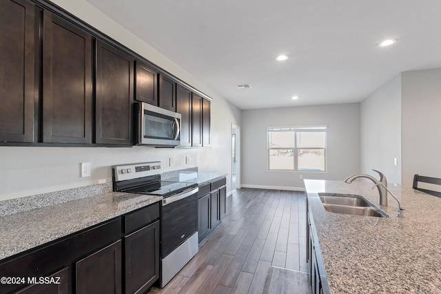 kitchen featuring dark brown cabinetry, wood finished floors, a sink, baseboards, and appliances with stainless steel finishes