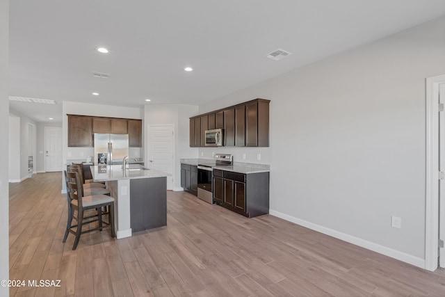 kitchen with light wood finished floors, visible vents, appliances with stainless steel finishes, a kitchen breakfast bar, and a sink