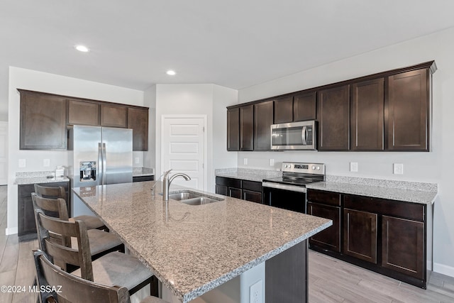 kitchen featuring dark brown cabinets, appliances with stainless steel finishes, a sink, and light stone countertops