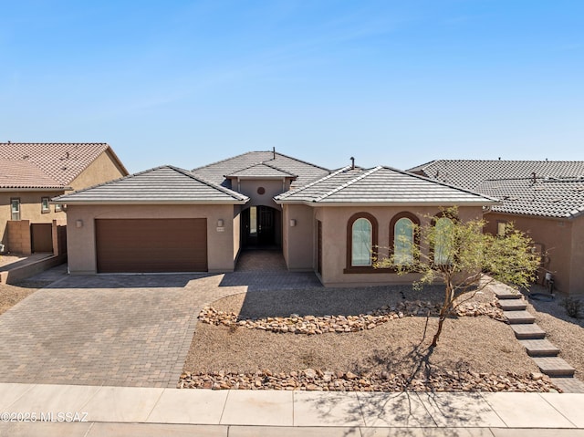 view of front facade featuring a tiled roof, decorative driveway, an attached garage, and stucco siding