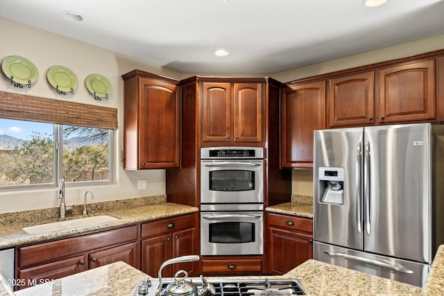 kitchen with appliances with stainless steel finishes, light stone counters, a sink, and recessed lighting