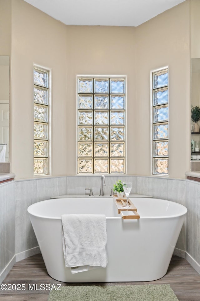 bathroom featuring a freestanding tub, wood finished floors, and wainscoting