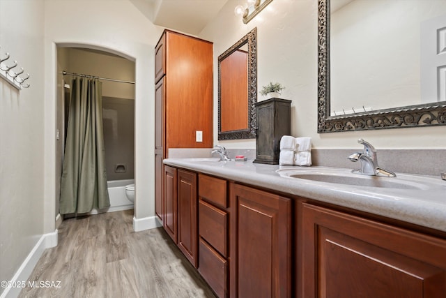 bathroom with double vanity, a sink, toilet, and wood finished floors