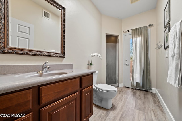 bathroom with visible vents, toilet, a stall shower, vanity, and wood finished floors