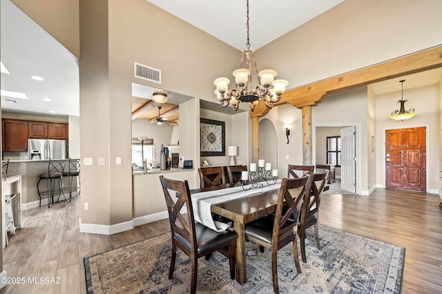 dining space with light wood finished floors, baseboards, visible vents, arched walkways, and a towering ceiling