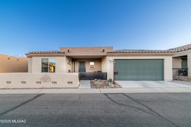 pueblo-style home featuring a garage, a fenced front yard, and stucco siding