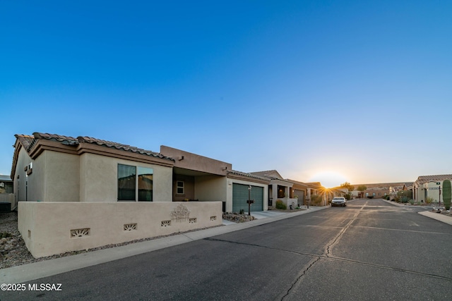 view of front of home featuring a garage, driveway, a tile roof, a residential view, and stucco siding