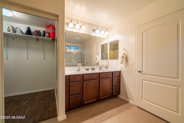 bathroom with double vanity, baseboards, a sink, and a shower with shower door