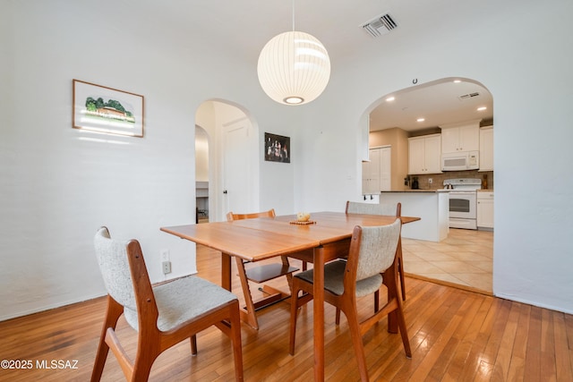 dining area with light wood-style floors, visible vents, and arched walkways