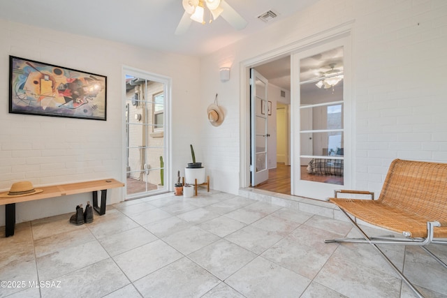 unfurnished room featuring visible vents, ceiling fan, brick wall, and light tile patterned floors