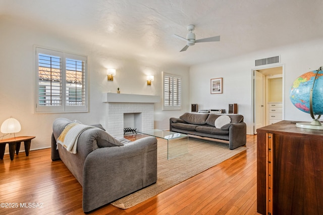 living room with a ceiling fan, a brick fireplace, visible vents, and hardwood / wood-style floors