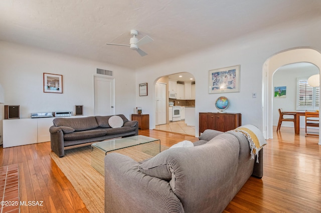 living room with arched walkways, ceiling fan, light wood-style flooring, and visible vents