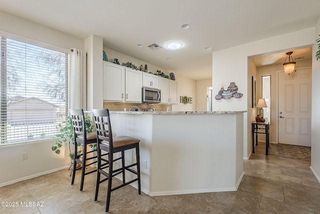 kitchen with visible vents, white cabinets, light stone countertops, tasteful backsplash, and stainless steel microwave