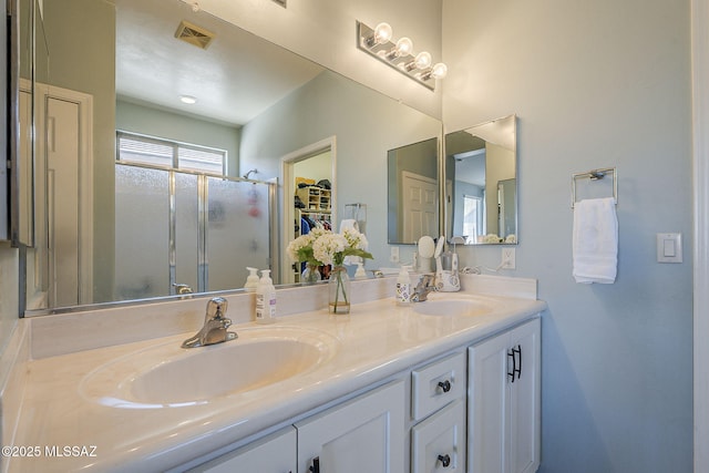 bathroom with double vanity, a stall shower, a sink, and visible vents