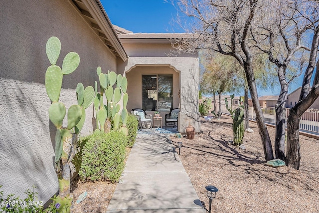 view of exterior entry featuring fence, a patio, and stucco siding