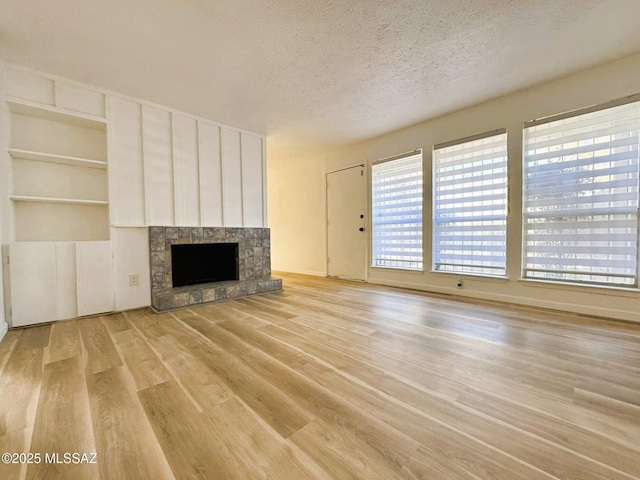 unfurnished living room with light wood-style floors, a fireplace with raised hearth, and a textured ceiling