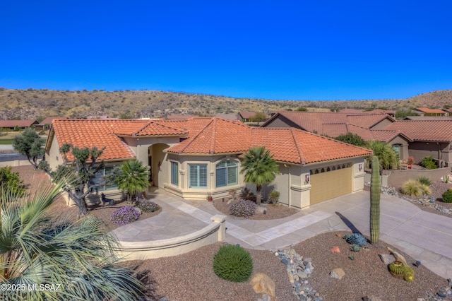 mediterranean / spanish-style home with a garage, a tiled roof, concrete driveway, and stucco siding