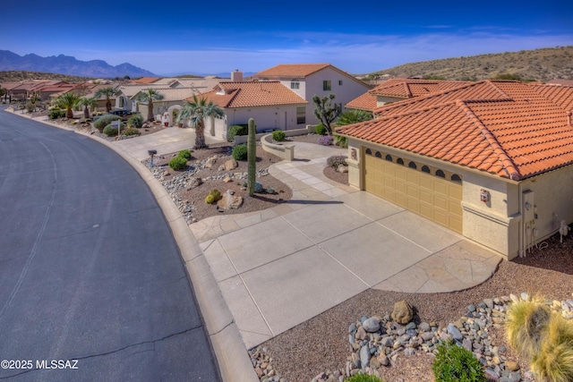 mediterranean / spanish-style home featuring a mountain view, a tile roof, concrete driveway, a residential view, and stucco siding