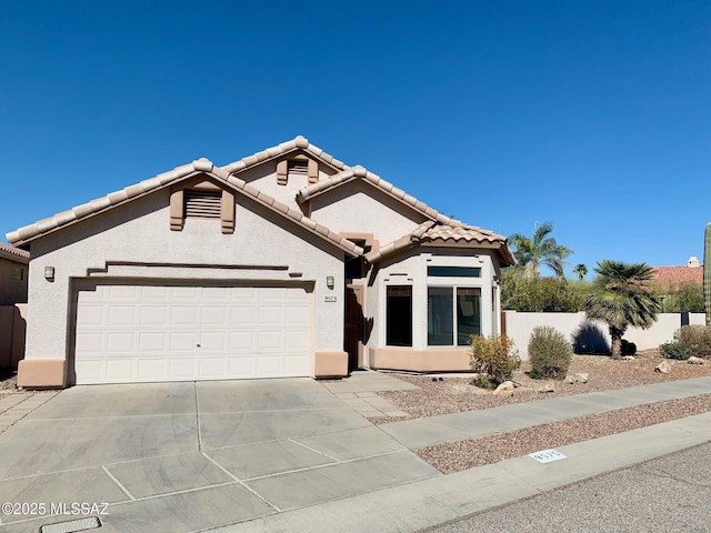 mediterranean / spanish-style house featuring concrete driveway, a tiled roof, an attached garage, fence, and stucco siding